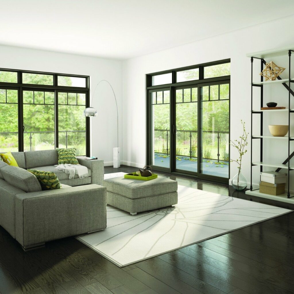 Salon moderne et lumineux avec canapé gris, grandes fenêtres et vue sur jardin verdoyant.
