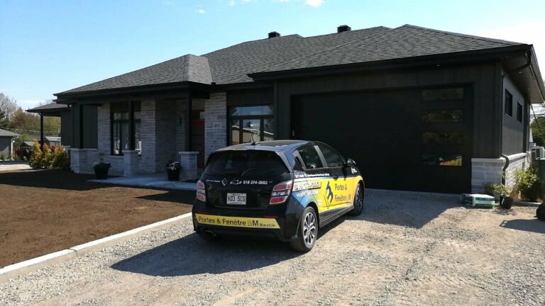 Voiture d'une entreprise de portes et fenêtres garée devant une maison moderne en briques et bois noir.