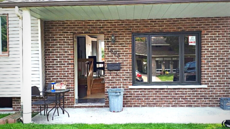 Entrée de maison en briques avec table et chaises extérieures devant une pelouse bien entretenue.