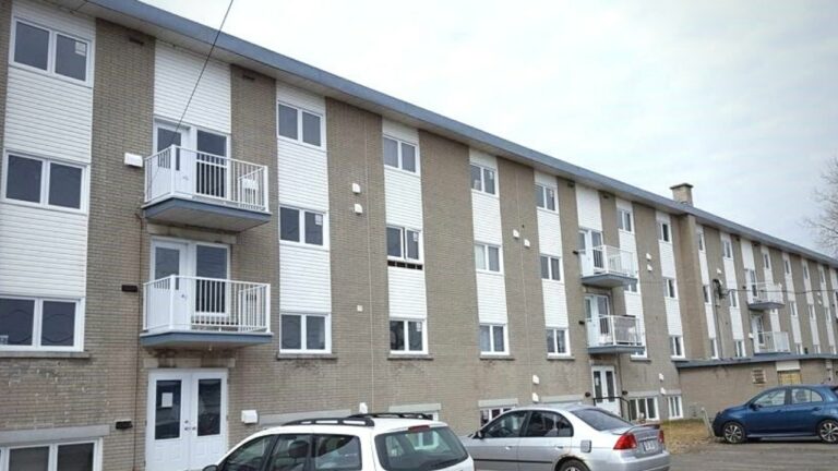 Immeuble résidentiel moderne à trois étages, avec balcons et voitures garées devant.