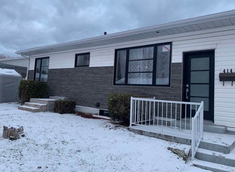 Maison moderne avec façade en briques, entourée de neige, ciel nuageux en arrière-plan.