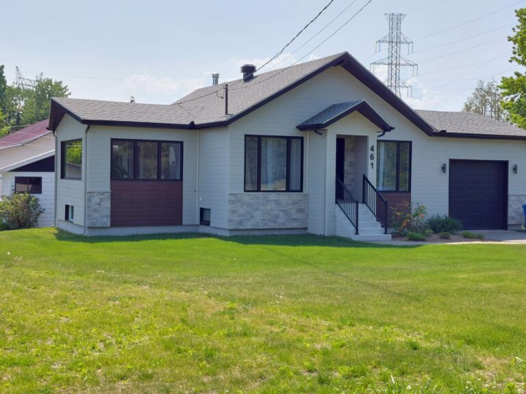 Maison moderne avec façade en pierre, pelouse verte, et garage intégré, située dans un quartier résidentiel calme.