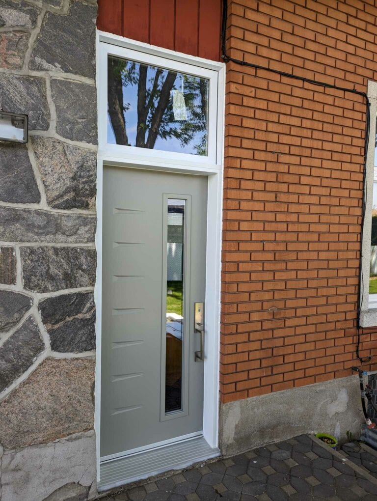 Porte moderne grise avec fenêtre en verre, encadrée par des murs en pierre et briques rouges.